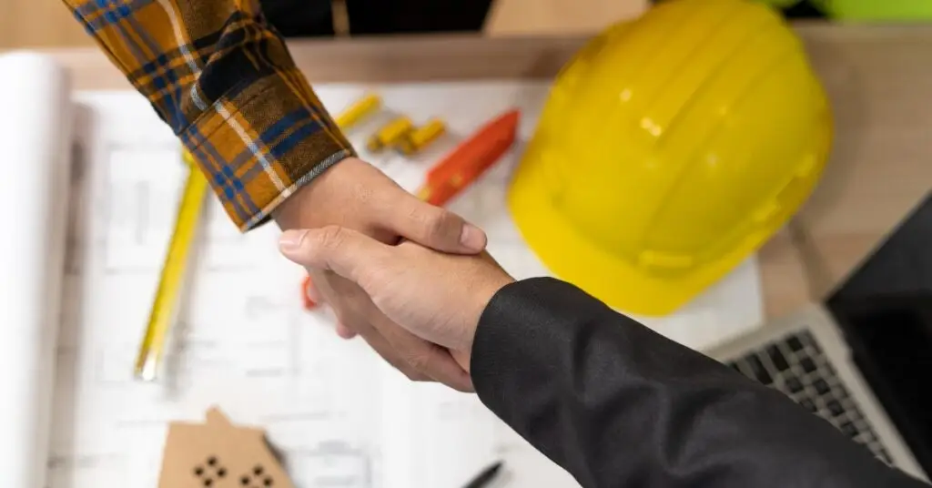 Handshake over architectural plans with a construction helmet, symbolising professional collaboration in planning permission for a driveway.