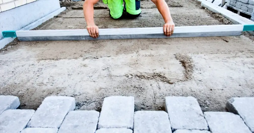 Worker using a spirit level on newly laid block paving for a driveway, ensuring perfect alignment and surface level.